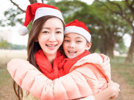 Photo for Happy mother and daughter hugging and wearing santa claus red hats - Royalty Free Image