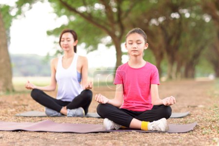 Téléchargez les photos : Mère et fille faisant des exercices de yoga sur l'herbe dans le parc - en image libre de droit