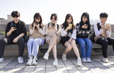 Téléchargez les photos : Joyeux jeune groupe utilisant les téléphones mobiles à l'école - en image libre de droit