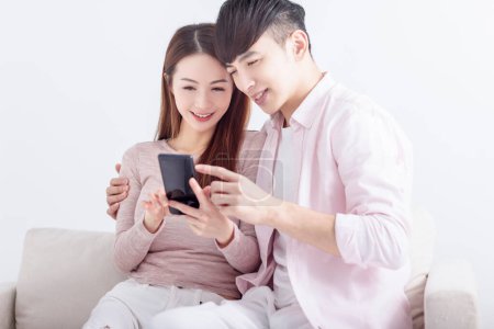 Photo for Young  couple using smart phone , browsing internet, chatting online, relaxing on sofa at home - Royalty Free Image