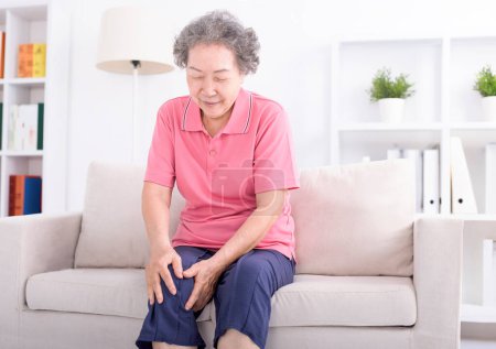 Téléchargez les photos : Asiatique senior femme assis sur canapé et ayant la douleur articulaire - en image libre de droit