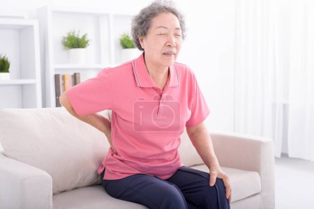 Foto de Mujer mayor que sufre de dolor de espalda en casa - Imagen libre de derechos