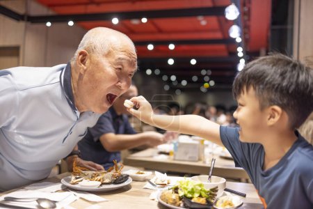 Téléchargez les photos : Heureux enfant nourrit grand-père avec des biscuits au restaurant - en image libre de droit