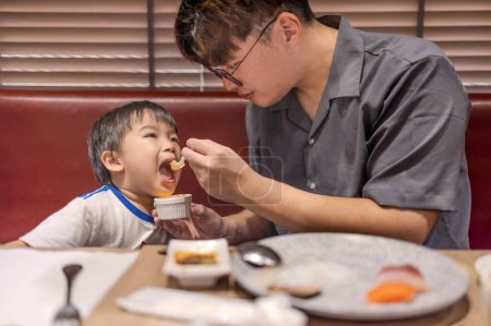 Photo for Happy father feeds her son in restaurant - Royalty Free Image