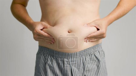 Téléchargez les photos : Gros plan de l'homme main pincer graisse du ventre excessive - en image libre de droit