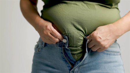 Foto de Mujer gorda abrochándose los pantalones, exceso de grasa abdominal, estilo de vida poco saludable - Imagen libre de derechos