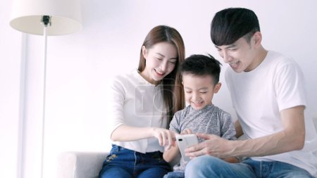 Photo for Happy parent and  kid using mobile phone, resting on home couch together - Royalty Free Image