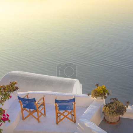 Téléchargez les photos : Santorin, Grèce. Deux chaises sur la terrasse donnant sur la mer et le coucher du soleil sur l'île de Santorin. Une époque romantique. Vacances en Grèce, Santorin. - en image libre de droit