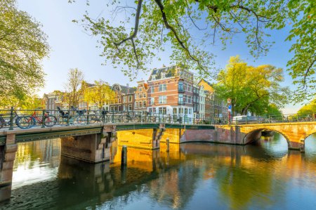 Foto de Ámsterdam bajo el sol de la mañana. Casas y puentes tradicionales de Ámsterdam. Hermosa mañana en Amsterdam. Holanda, Países Bajos, Europa. - Imagen libre de derechos
