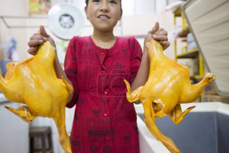Foto de Tupiza, Bolivia - 30 de diciembre de 2014: Joven asiática sonriendo y sosteniendo dos pollos a la venta dentro de una tienda local en Tupiza, Bolivia - Imagen libre de derechos