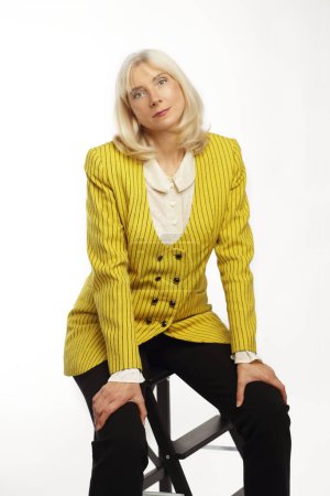 Beautiful blond lady in her 50s wearing yellow jacket posing over white background
