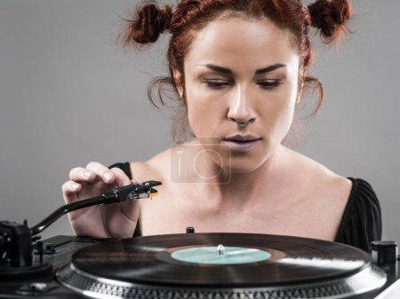Photo for Beautiful woman about to put the needle down on the vinyl record spinning on her record player. - Royalty Free Image