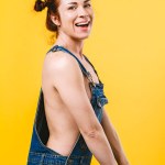 Sexy topless redhead woman laughing and wearing overalls over yellow background.