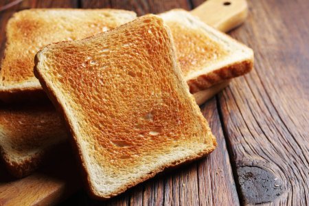 Photo for Slices of toasted bread on kitchen board on wooden table close up - Royalty Free Image