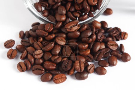 Roasted coffee beans scattered from a glass jar on a white background close-up