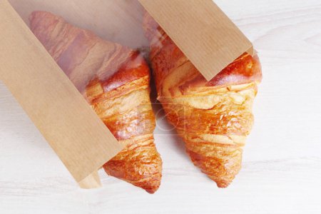 Foto de Croissants en una bolsa de papel en una mesa de luz de cerca, vista superior - Imagen libre de derechos
