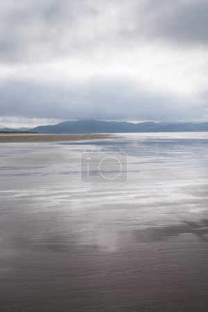 Foto de Amplia playa vacía en un día nublado con cielo nublado reflejándose en arena mojada. Inch Beach, Wild Atlantic Way, Condado de Kerry, Irlanda. - Imagen libre de derechos