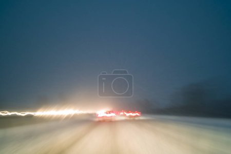 Téléchargez les photos : Conduite dans de mauvaises conditions météorologiques avec neige sur l'autoroute de nuit, flou de mouvement avec des sentiers lumineux créés par la photographie de longue exposition - en image libre de droit