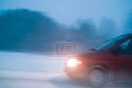 Téléchargez les photos : Voiture conduisant dans des conditions météorologiques défavorables avec neige sur l'autoroute de nuit, longue exposition dans le flou du mouvement de la caméra - en image libre de droit