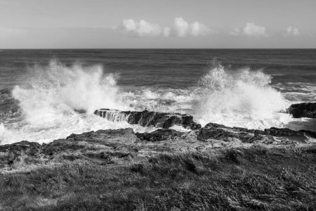 Poderosas olas aplastándose sobre rocas en la costa atlántica de Irlanda, en blanco y negro.