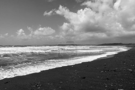 Powerful waves in stormy ocean seen from sandy beach of Atlantic coast of Ireland on windy day, in black and white.