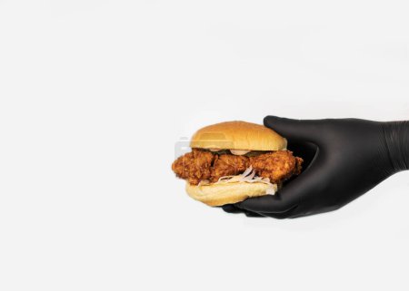 Foto de Una jugosa hamburguesa artesanal con queso se lleva a cabo en manos de un chef con guantes negros sobre fondo blanco - Imagen libre de derechos