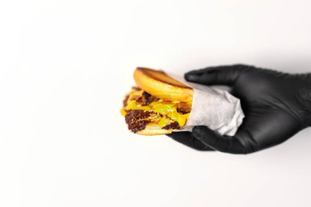 Téléchargez les photos : Un hamburger juteux artisanal au fromage est tenu dans les mains d'un chef en gants noirs. - en image libre de droit