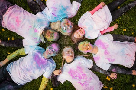 Foto de Grupo de personas felices celebrando Holi con colores en polvo o gulal. Acostado en la hierba, vista superior. Concepto de festival indio Holi. - Imagen libre de derechos