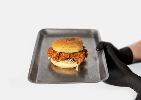 Foto de Una jugosa hamburguesa artesanal con queso se lleva a cabo en manos de un chef con guantes negros sobre fondo blanco - Imagen libre de derechos