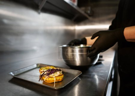 Téléchargez les photos : Burger juteux artisanal au fromage est fabriqué par un chef portant des gants noirs sur fond de cuisine. - en image libre de droit