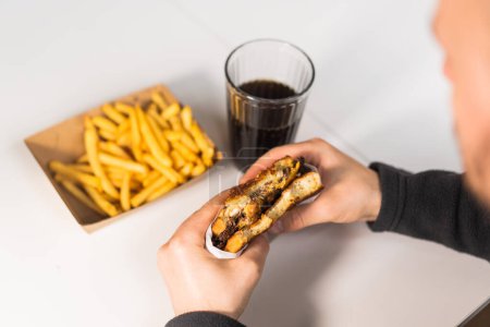 Photo for The guy is holding a burger in his hand, cola and fries on the table - Royalty Free Image
