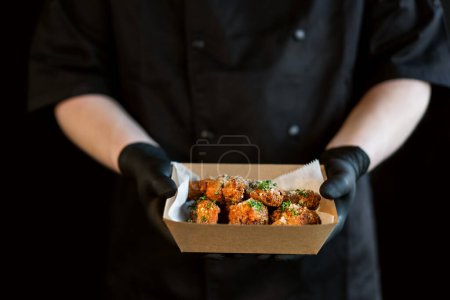 Téléchargez les photos : Le cuisinier tient dans ses mains une boîte de poulet épicé grillé teriyaki jambes dans des paquets pour la livraison. - en image libre de droit
