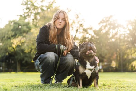 Photo for A young teenage girl hugs her French bulldog dog in a park on the grass. - Royalty Free Image