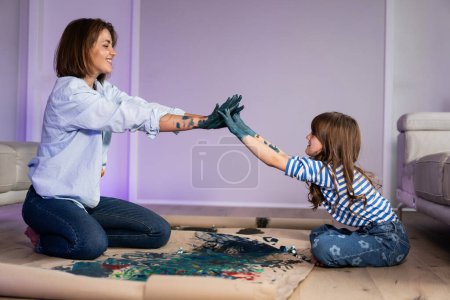 Téléchargez les photos : Maman et fille peignent ensemble sur le sol sur du carton avec des peintures à l'huile avec leurs mains - en image libre de droit