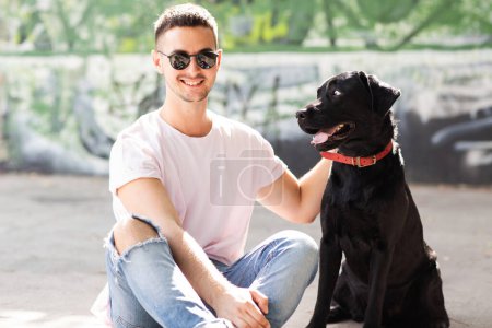 Photo for Guy in sunglasses hugs his dog in autumn park at sunset - Royalty Free Image