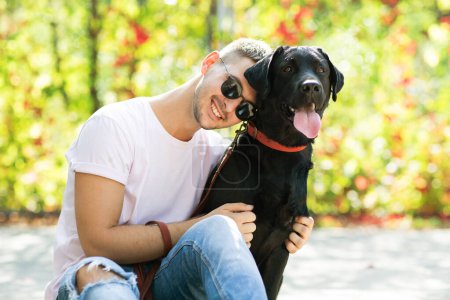 Foto de Guy en gafas de sol abraza a su perro en el parque de otoño al atardecer - Imagen libre de derechos