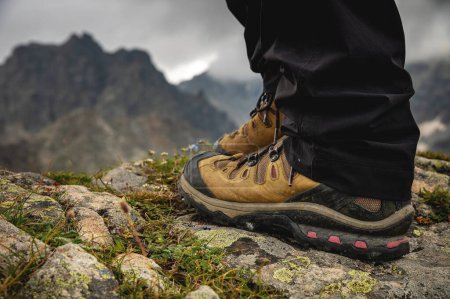 Téléchargez les photos : Close-up of legs in trekking boots against the backdrop of an alpine mountain range in a valley. - en image libre de droit