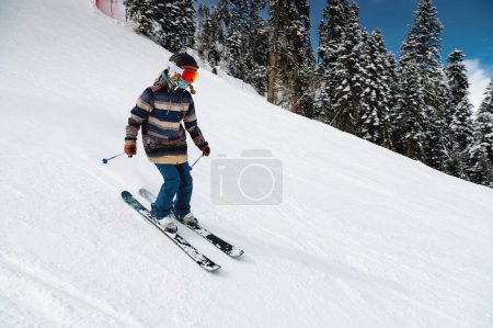 Foto de A woman skier in a ski resort quickly descends the track against the backdrop of the forest and sky. - Imagen libre de derechos
