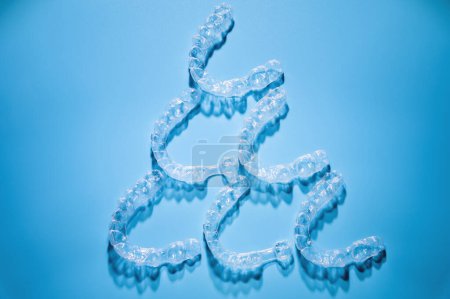 Foto de Close up, invisible aligners on a blue background in the shape of a pyramid or triangle creating a pattern. Plastic braces for teeth alignment. - Imagen libre de derechos