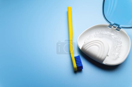 Téléchargez les photos : Transparent braces in a special storage box with a toothbrush lie on a blue background, close-up. daily dental care concept. - en image libre de droit