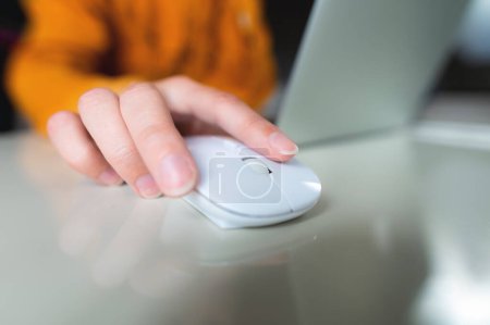 From above, close-up photo of a hand with a wireless white computer mouse to search for the necessary information, on the desktop.
