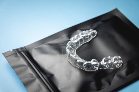 Nahaufnahme, unsichtbare Kunststoffspange auf einer schwarzen Spezialverpackung mit Reißverschluss, die auf blauem Hintergrund liegt. Studioaufnahme, Hintergrund Zahnklinik.
