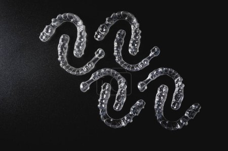 Foto de Un patrón de alineadores de plástico invisibles se encuentran sobre un fondo negro. - Imagen libre de derechos