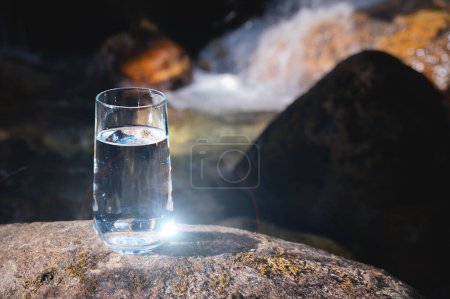 Natural drinking water in a glass glass on the background of the nature river. Sunlight reflects on the glass showing clear clear water..