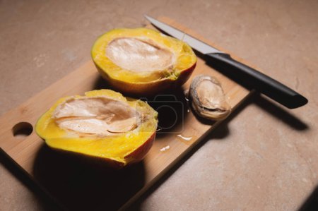 Foto de Mango amarillo y gran hoyo en una tabla de cortar en la mesa de la cocina. Semillas frescas de mango maduro y primer plano de fruta. Residuos de cocina biodegradables para el reciclaje. Desperdicio. Primer plano. - Imagen libre de derechos