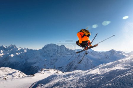 Foto de El esquiador salta sobre el fondo del cielo azul y las montañas cubiertas de nieve. freestyle esquiador realiza helicóptero con esquís cruzados simultáneamente con rotación completa. - Imagen libre de derechos