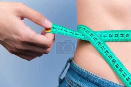 Eine Frau misst ihre Taille mit einem Maßband. Ernährungs- und Körpergewichtskontrolle, hautnah, durchtrainiert. Ein Mädchen in Jeans misst ihre Figur und ihren Gewichtsverlust