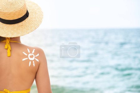 Eine Frau trug Sonnencreme auf ihre gebräunte Schulter in Form einer Sonne auf. Sonnenschutz. Sonnencreme. Haut- und Körperpflege