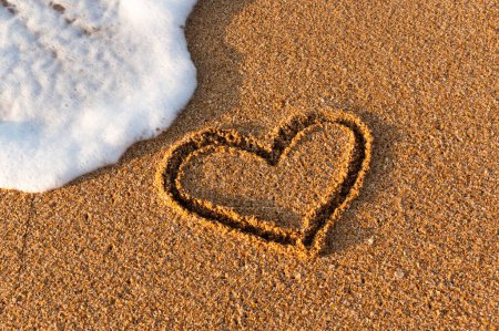 Corazón dibujado en la arena en la playa al atardecer. Forma de corazón. Símbolo del corazón. Amor. Espuma marina.