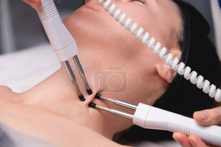 Nahaufnahme einer Frau, die in einem Schönheitssalon eine elektrische Nackenmassage mit Geräten erhält. Zur Therapie mit einem multifunktionalen Elektromassagegerät.